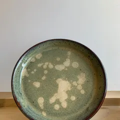A handmade dinner plate with a beautiful, speckled green glaze. The abstract white splashes add a touch of modern artistry to this functional piece.