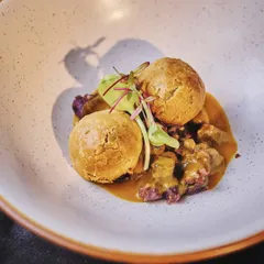 A beautifully plated version of litti chokha. Here, feta and amaranth puff "litti" are served on a bed of purple potato chokha and drizzled with artisanal ghee, elevating a rustic dish to gourmet heights.