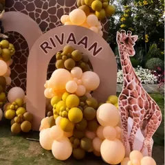 A modern and earthy jungle theme setup, using muted yellow and olive green balloons with a giraffe-print arch and a large giraffe cutout.