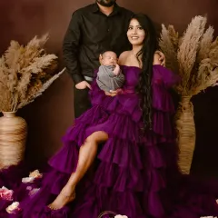 A beautiful first family portrait. The mother is seated in a stunning purple gown, holding her newborn, with her partner standing behind, creating a classic composition.