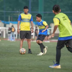 A coach observes a young player's technique closely during a drill. This image embodies our belief that behind every confident young player is a coach who believed in them first.