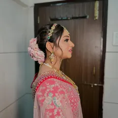 A classic bridal bun made romantic with a garland of fresh pink roses. This style is perfect for the main ceremony, keeping the hair elegantly off the face while adding a soft, floral touch to the overall look.