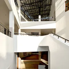 This interior view showcases the multi-level, open-air corridors at Vidyamandir School. The design, featuring a large overhead skylight and exposed structural elements, allows for constant air circulation and diffused natural light, eliminating the need for artificial lighting in common areas during the day.