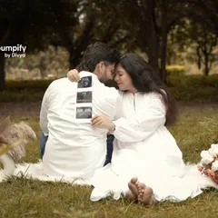 A sweet and intimate moment during an outdoor picnic-style shoot. The couple, dressed in white, shares a quiet moment while holding up their baby's first pictures, the sonogram.