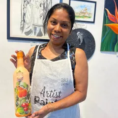 A participant with her finished decoupage bottle, decorated with a vibrant fruit pattern. This workshop teaches you how to upcycle old bottles into beautiful decorative items.