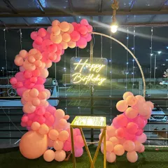 A vibrant pink balloon semi-arch on a rooftop. The neon 'Happy Birthday' sign glows beautifully against the evening sky, creating a perfect party atmosphere.