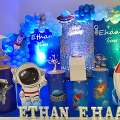 An out-of-this-world space and astronaut theme for a joint birthday party. This design uses cool blue lighting, a sparkling sequin wall, and themed props like astronauts, rockets, and a crescent moon to create a cosmic adventure.