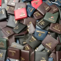 A look at the wide variety of personalized wallets I have crafted. You can see different colors like red, blue, brown, and green, and various charms including crowns, hearts, and wings, ready for my customers.