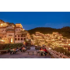 A blue-hour shot of the illuminated fort, capturing the serene and enchanting atmosphere of the evening as guests dine on the terrace. This is a classic example of luxury hotel photography.
