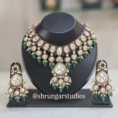 A classic and elegant Kundan bridal set that never goes out of style. This necklace and earring set features large, uncut polki-style stones, beautifully contrasted with deep green and ruby-red beads. It's a versatile choice that complements a wide range of bridal lehengas and sarees.