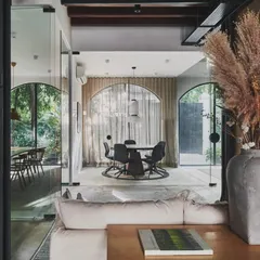 The ethereal lightness of our studio space, where sunlight paints nature’s hues across the room. Glimpses of vibrant trees outside are framed by large glass walls, blurring the line between inside and out.