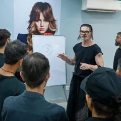 Education at our academy goes beyond practical work. Here, Bill Watson uses a whiteboard to break down the theory behind a haircut, ensuring our students grasp the foundational principles of structure and shape.