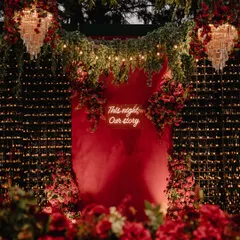 For this sangeet night, we went for bold, immersive romance. A custom neon sign with the couple's words, "This night, Our story," glowed against a dramatic backdrop of red florals, chandeliers, and a wall of candles, creating an electric atmosphere.