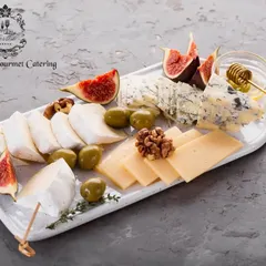 A pristine white platter showcasing a selection of fine cheeses, including creamy brie, sharp blue cheese, and sliced swiss. Fresh figs and green olives add color and complementary flavors.