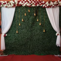 A simple and elegant traditional backdrop, combining a green grass wall with white drapes, a floral header, and hanging temple bells.