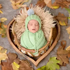 A heart full of love. This newborn, wrapped in a cozy green knit, sleeps peacefully in a heart-shaped wooden bowl amidst autumn leaves.