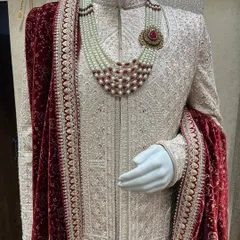 A closer look at the royal treatment. This ivory sherwani features detailed embroidery, paired with a rich red velvet stole and a multi-layered pearl necklace. I focus on these details to give you a truly regal look for your wedding day.