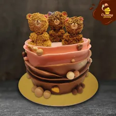 This unique cake features three incredibly detailed teddy bears made from piped chocolate frosting, giving them a fuzzy, textured look. The cake itself has a modern chocolate-wrapped design in shades of brown and pink.