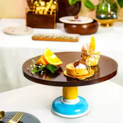 A vibrant wooden and ceramic cake stand styled with pastries on a fully set table. This shot shows the product in its intended environment, surrounded by other complementary tableware.