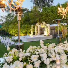 A view of the stunning outdoor setup for the anniversary, with a white floral stage, elegant seating, and chandeliers creating a magical garden party atmosphere.