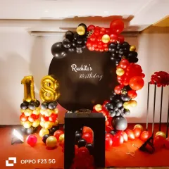 A bold and glamorous 18th birthday celebration. The decor uses a striking red, black, and gold color scheme with a balloon arch over a personalized black backdrop.