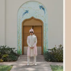 A full-length portrait of the groom looking sharp and stylish in his wedding attire, standing before a beautifully painted archway.