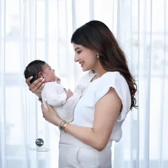 A mother gazes lovingly at her newborn baby, holding her by a window with soft, natural light. This is a perfect example of a simple, beautiful moment from a lifestyle session.