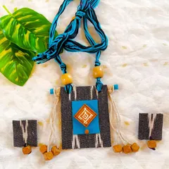 This necklace set features grey Ikat fabric paired with a bright turquoise, hand-painted square. The design is accented with wooden beads and jute tassels for a rustic, contemporary feel. The adjustable cord is braided from blue and black threads.