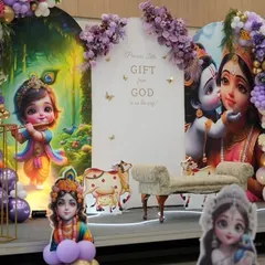 A beautiful baby shower stage in a purple and gold color scheme. The decor includes custom backdrops with Krishna illustrations, a sign that reads 'Precious Little Gift From God', and a small chaise lounge for the mother-to-be, all surrounded by purple and gold balloons.