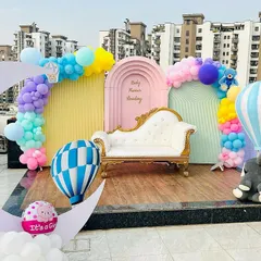 We create beautiful memories with our themed baby shower decorations, even on a rooftop. This setup includes a pastel color palette, a large crescent moon prop, hot air balloon models, and a comfortable lounge seat for the parents to be, all set against a city skyline.