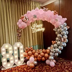 A beautiful 80th birthday party featuring a circular balloon arch in pink, rose gold, and silver, complemented by large marquee numbers and a neon sign.
