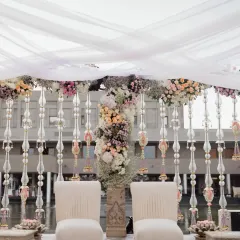 A serene and breezy engagement setup at the Intercontinental Hotel, Mahabalipuram. The design features a mandap with clean lines, draped in sheer white fabric and adorned with pastel floral arrangements, all set against a tranquil water body.