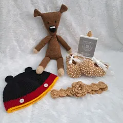 A complete character-themed gift set for a special baby. This hamper features a Mickey Mouse inspired beanie, a pair of brown beaded booties with a matching floral headband, and a cuddly amigurumi teddy bear inspired by Mr. Bean's Teddy.