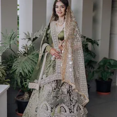 A bride looking radiant in our olive green lehenga. The intricate silver and white embroidery stands out beautifully against the deep green fabric, offering a unique and elegant choice for a wedding or reception.