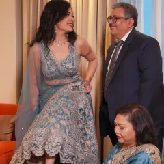 A beautiful family moment. The bride shares a laugh with her father while her mother helps with her shoes, a candid scene full of love and warmth.
