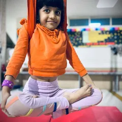 A young student finds her center, sitting in a perfect lotus pose while suspended in the aerial hammock.