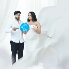 A fun gender reveal photo with an expecting couple. They point to a blue balloon that says "It's a Boy," sharing their exciting news in a beautiful studio setting.