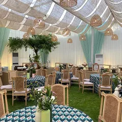 A minimalist and chic outdoor event setup. The design uses natural textures like jute drapes, rattan chairs, and printed linens to create a sophisticated yet relaxed atmosphere perfect for a modern, understated celebration.