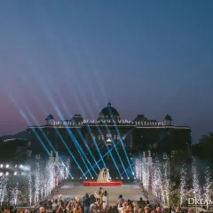 As dusk settles, the entire palace facade becomes a canvas for light and celebration. This wide shot captures the sheer scale and cinematic quality of the Varmala ceremony I designed.
