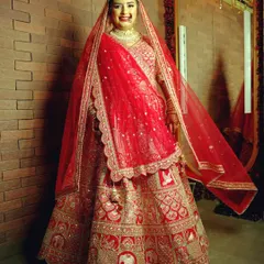 The classic full-length bridal portrait. This shot showcases the bride's entire stunning red lehenga, with its intricate elephant motifs, against a simple brick wall that makes the outfit's colors and details stand out.