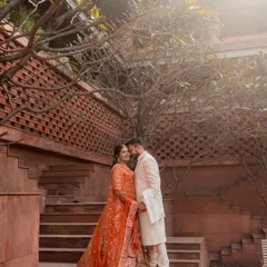 A romantic portrait on the terracotta steps of the resort. The warm tones of the architecture complement the bride's orange lehenga, and the surrounding trees frame the couple beautifully.