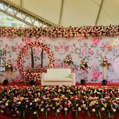This is a lavish floral stage created for a large reception. The backdrop features a floral print wall, a full floral ring, and a stage lined with a dense arrangement of multi-colored flowers.