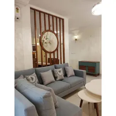 A closer look at the living area, where the custom L-shaped sofa and wooden partition create distinct zones while maintaining an open, airy feel. The mix of patterned and solid cushions adds a layer of texture and personality.