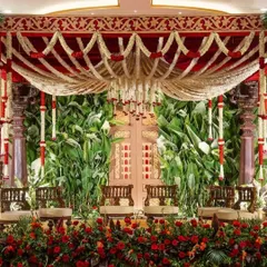 A truly magnificent South Indian wedding mandap that honors tradition with its grandeur. The lush green backdrop contrasts beautifully with the rich red and white floral garlands, creating a sacred and visually stunning space for the ceremony.