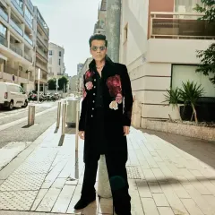 Karan Johar wearing a custom black longline jacket with bold, hand-embroidered floral motifs in shades of red and pink. This Indowestern piece is crafted from rich velvet for a truly luxurious feel.