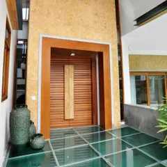 The entrance to this home features a glass floor over a water channel, creating a unique and memorable arrival experience. The oversized wooden door is framed by natural stone, blending modern design with earthy materials.
