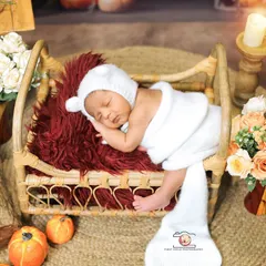 A cozy and rustic scene for a sleeping newborn. Dressed in a white bear bonnet, the baby is nestled in a miniature wooden bed, surrounded by warm candlelight and autumnal props for a storybook feel.