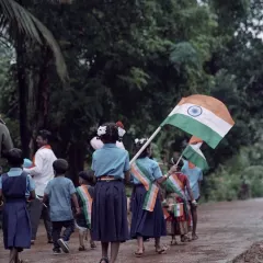 The same group of children seen from behind as they walk down a wet village road. This perspective feels more candid and observational, focusing on their collective journey.