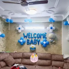 A classic 'Welcome Baby' boy decoration for a living room. The setup includes blue and white balloons, flower-shaped balloon clusters, and 'WELCOME BABY' foil letters.