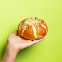 A single, perfect Korean Cream Cheese Bun, showcasing its golden-brown crust and cheesy topping. It's the ultimate savoury snack.